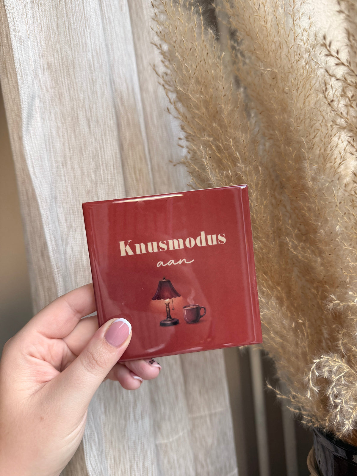 Tegel met tekst Knusmodus aan op dieprode achtergrond met lamp en mok
