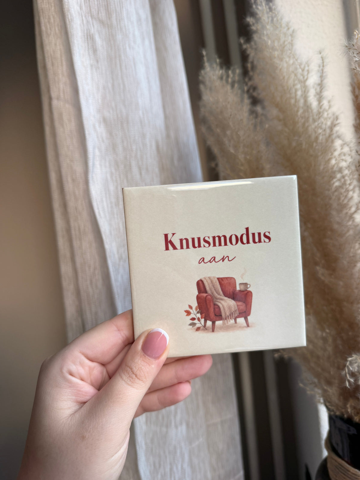 Tegel met tekst Knusmodus aan met rode fauteuil plaid en mok