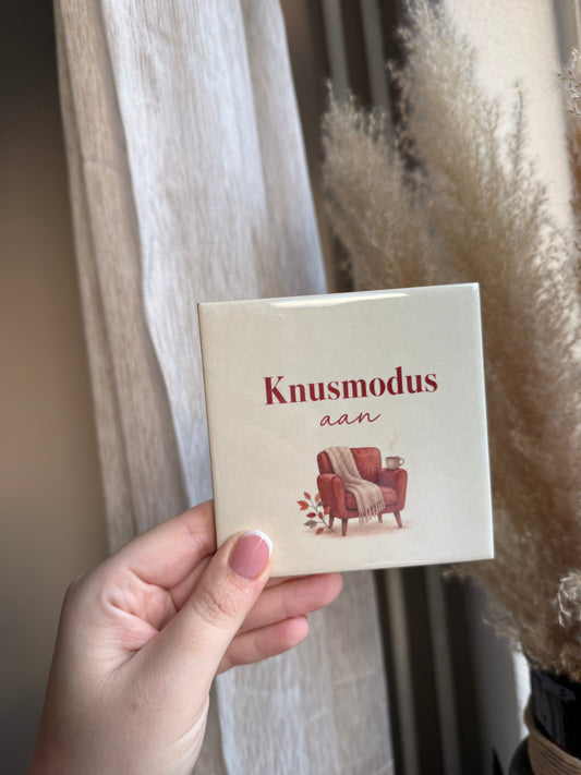Tegel met tekst Knusmodus aan met rode fauteuil plaid en mok